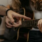 Dłonie nauczyciela i ucznia ustawiają palce na gryfie gitary