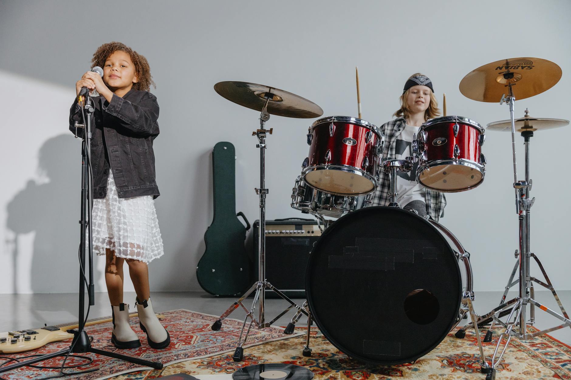 Dwójka dzieci grających w zespole: mikrofon i perkusja w sali indoors
