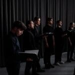 Jak czytać linię melodyczną, gdy śpiewasz harmonię w chórze Chór w czarnych strojach ćwiczy w sali, trzymając nuty w rękach