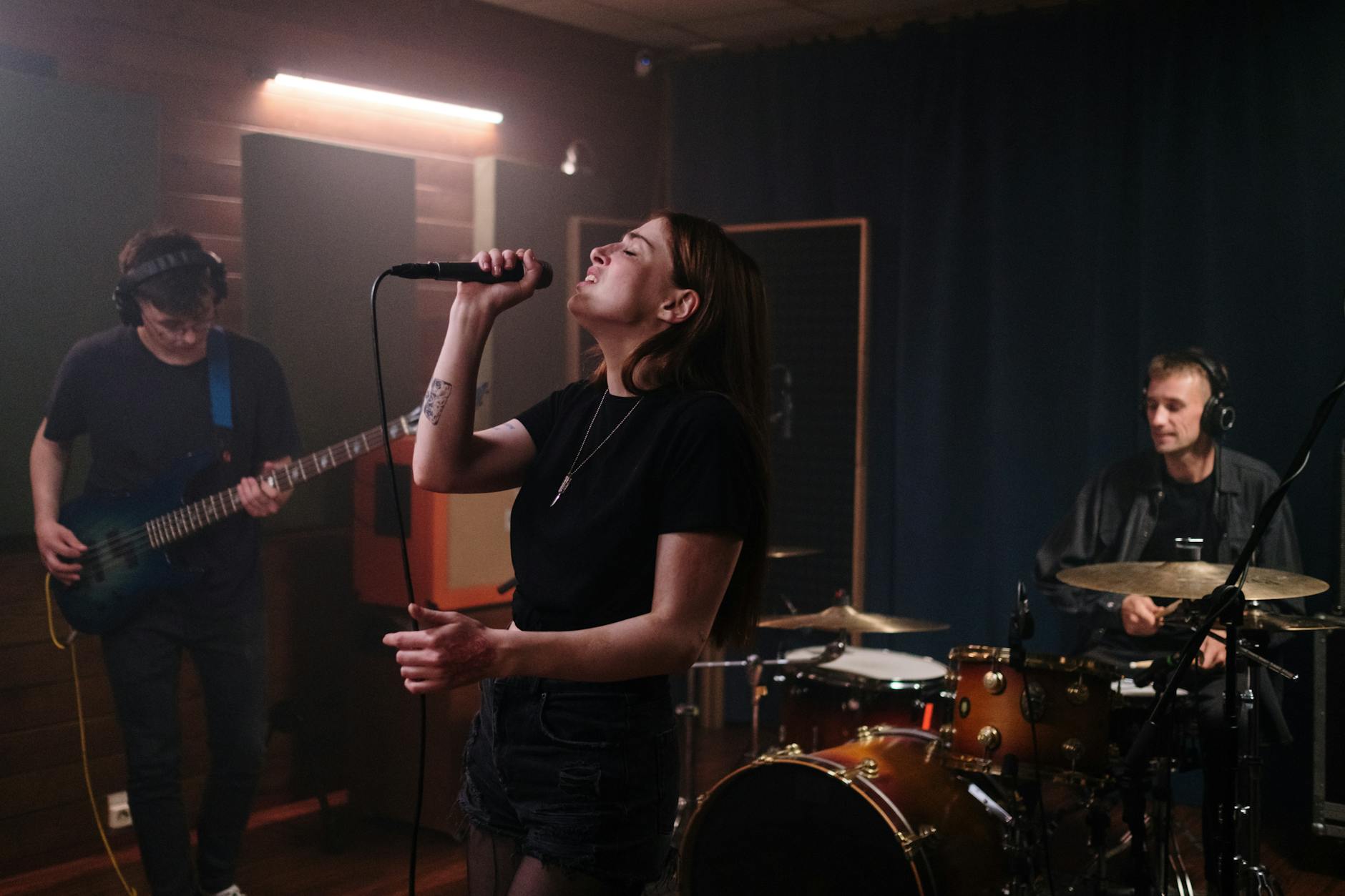 Zespół indie ćwiczący w sali: wokalistka, gitarzysta i perkusista