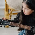 Dziewczynka stroi ukulele podczas nauki gry w domu