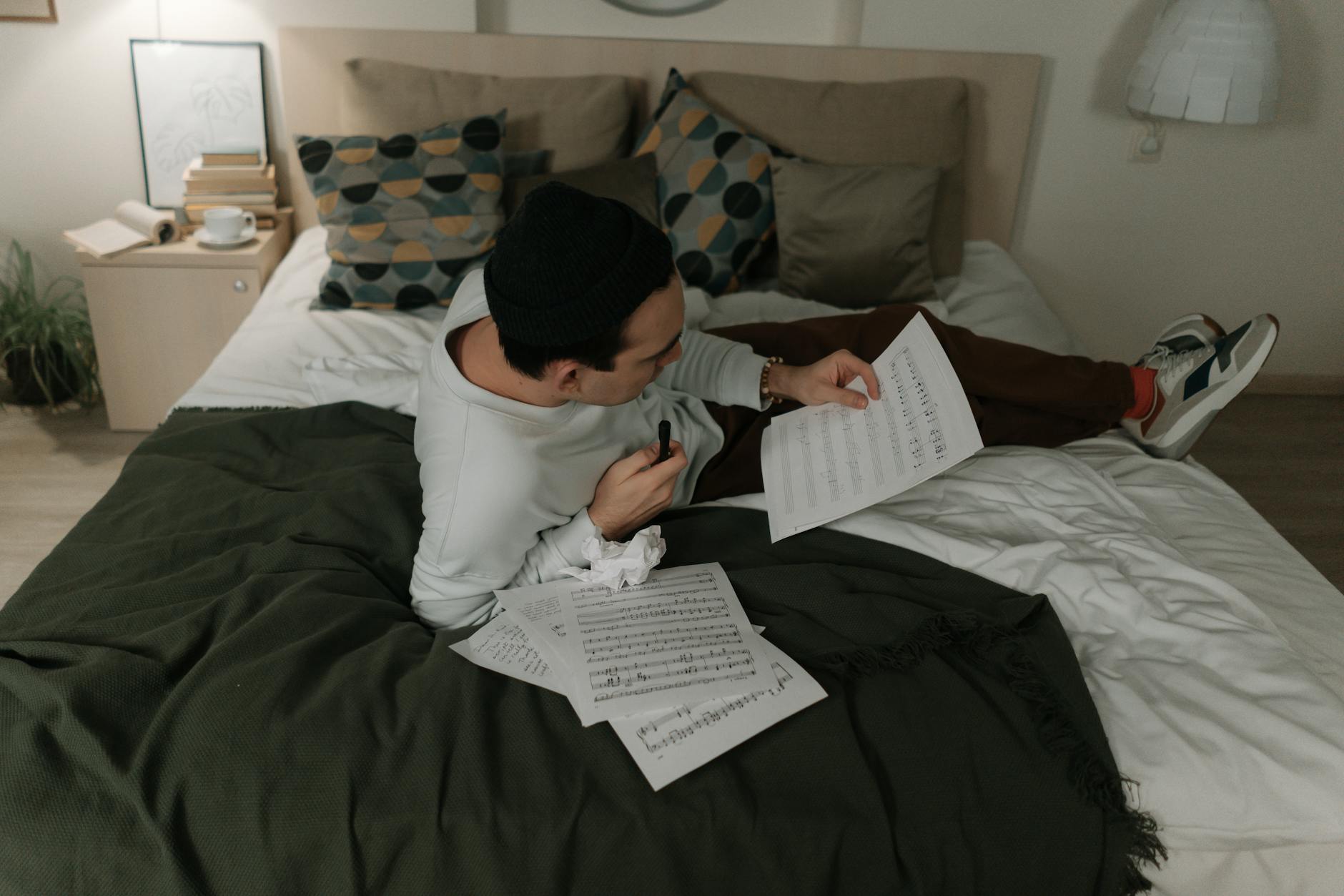 Mężczyzna na łóżku komponuje muzykę, otoczony nutami i przytulnym wystrojem