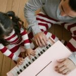 Tata i córka grają razem na różowym zabawkowym pianinie w domu