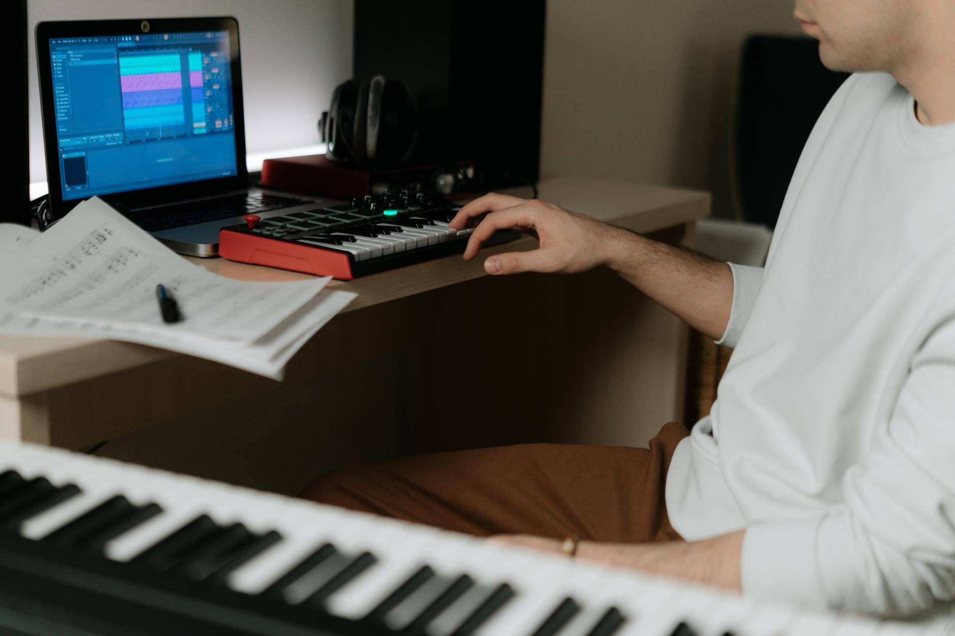 Osoba produkująca muzykę na klawiaturze MIDI i laptopie w domowym studiu