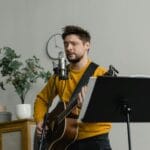 Wokalista z gitarą ćwiczy śpiew przy mikrofonie w sali muzycznej