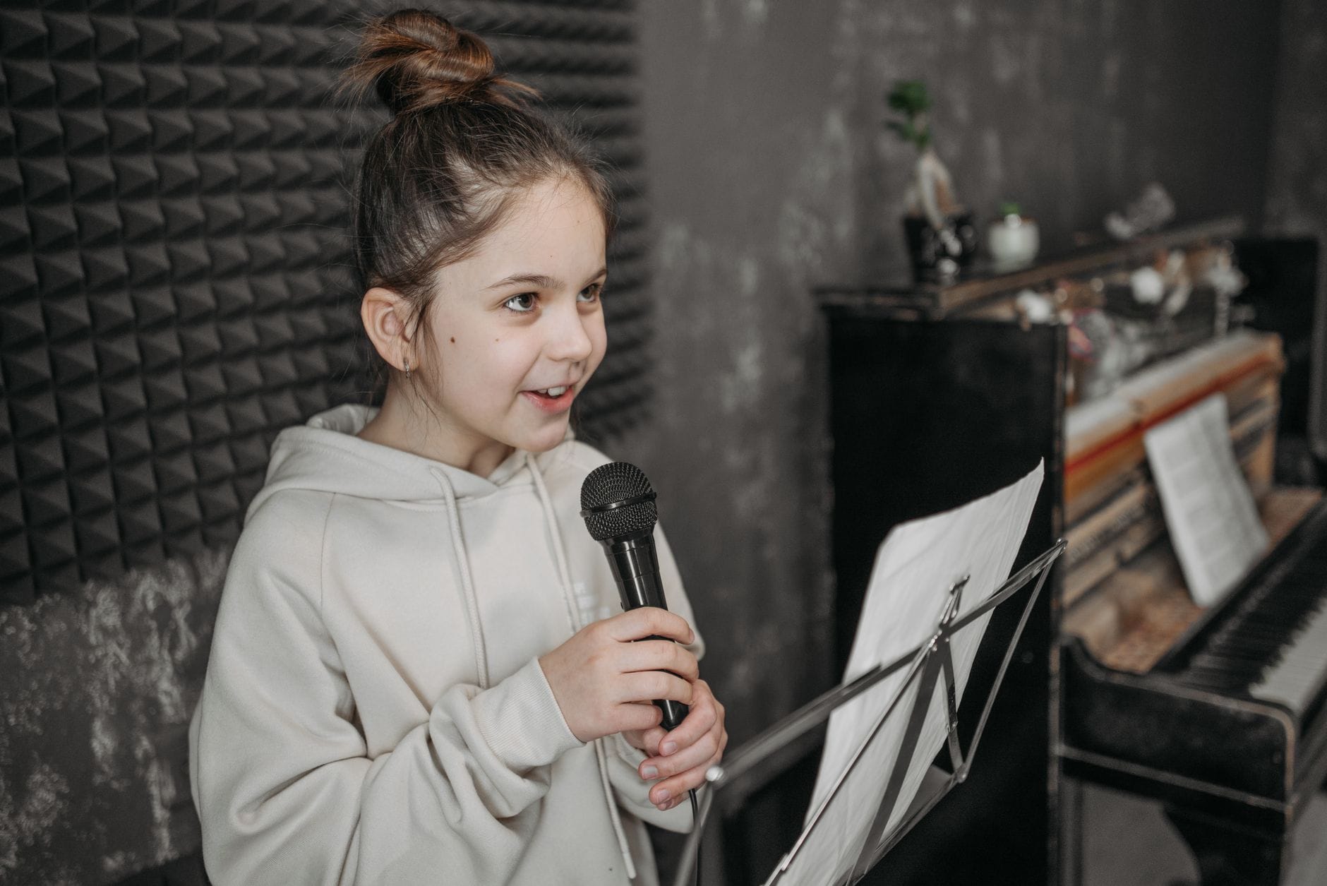 Młoda wokalistka śpiewa do mikrofonu w studiu nagrań przy pianinie