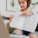 Kobieta prowadząca lekcję muzyki online z gitarą i nutami