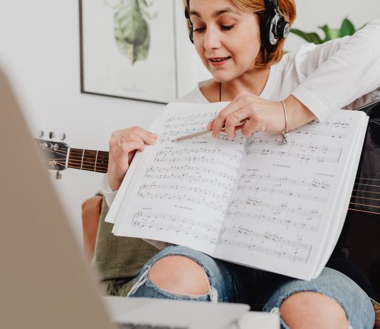 Darmowe programy do pisania i odtwarzania nut – MuseScore czy Finale Notepad? Kobieta prowadząca lekcję muzyki online z gitarą i nutami